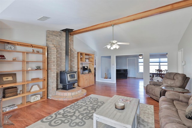 living room featuring hardwood / wood-style floors, vaulted ceiling with beams, a wood stove, and ceiling fan