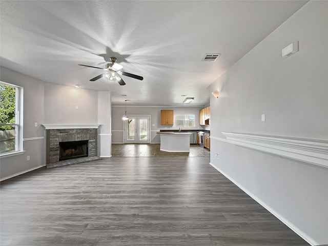 unfurnished living room with ceiling fan, a stone fireplace, dark wood-type flooring, and french doors