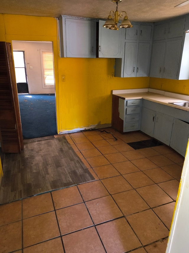 kitchen with pendant lighting, sink, tile patterned flooring, a textured ceiling, and a chandelier