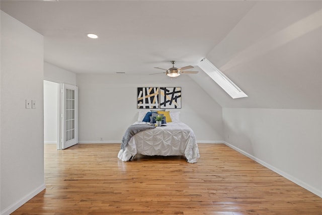 bedroom with light wood-type flooring, lofted ceiling with skylight, and ceiling fan