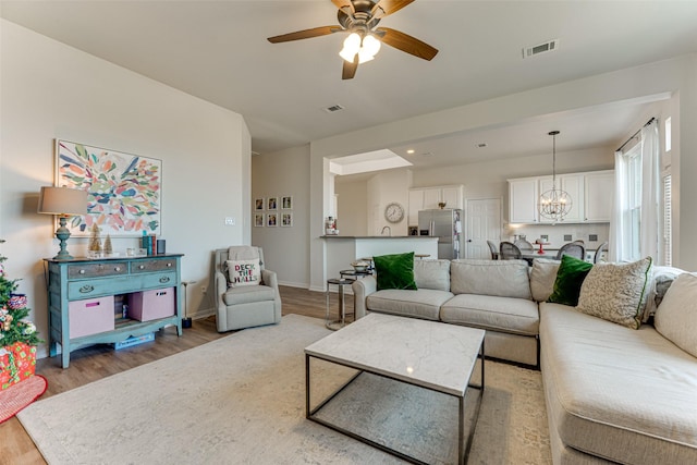 living room with light hardwood / wood-style floors and ceiling fan with notable chandelier