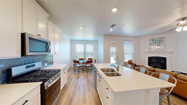 kitchen with appliances with stainless steel finishes, an island with sink, sink, white cabinets, and a kitchen breakfast bar