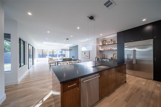 kitchen featuring a kitchen island with sink, hanging light fixtures, sink, light hardwood / wood-style flooring, and appliances with stainless steel finishes