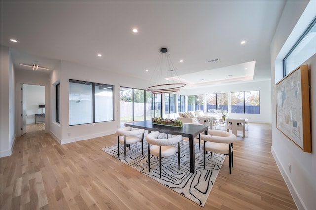 dining room with a raised ceiling, a notable chandelier, and light wood-type flooring