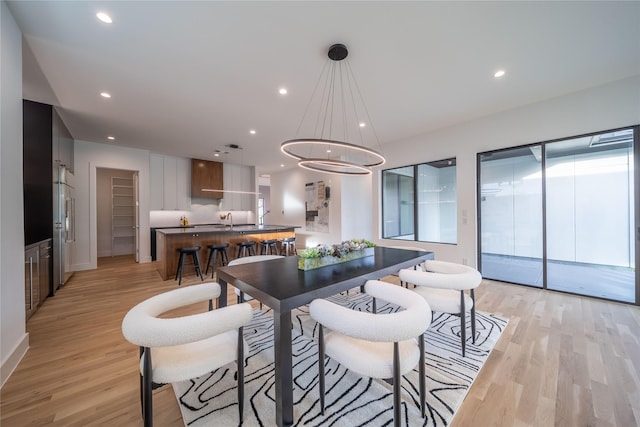 dining space featuring light wood-type flooring, sink, and an inviting chandelier