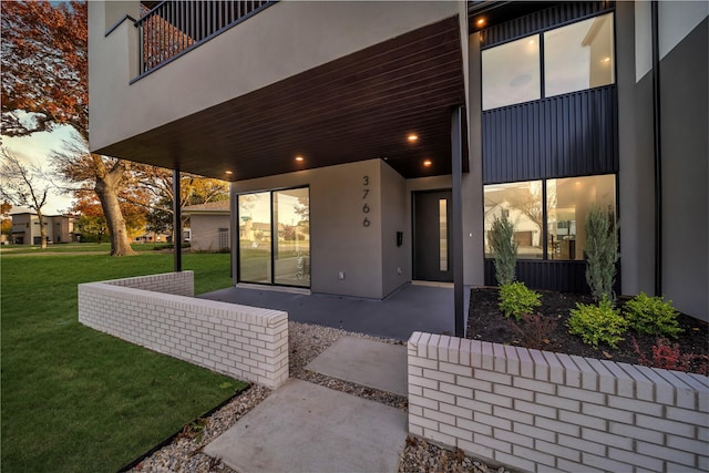 doorway to property with stucco siding, a lawn, and a patio area