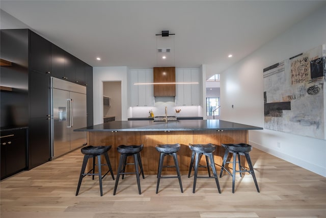 kitchen featuring a breakfast bar, built in fridge, light hardwood / wood-style flooring, and a kitchen island with sink