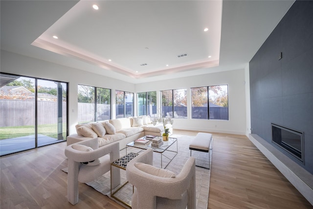 living room with a tile fireplace, light hardwood / wood-style floors, plenty of natural light, and a tray ceiling