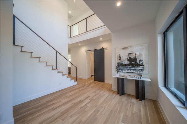 foyer entrance featuring a barn door, a towering ceiling, and light hardwood / wood-style flooring