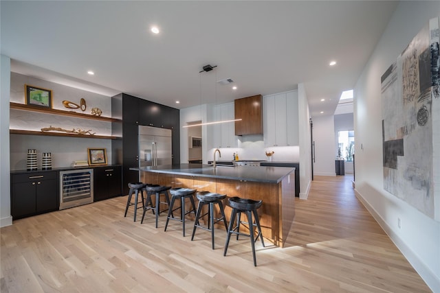 kitchen featuring a center island with sink, light hardwood / wood-style floors, hanging light fixtures, and beverage cooler