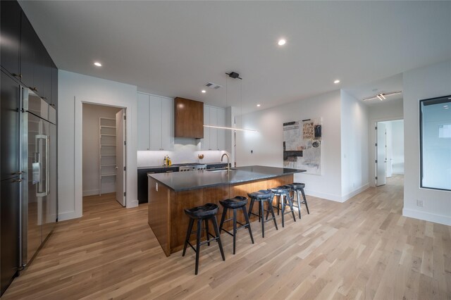 kitchen featuring light wood-type flooring, stainless steel built in fridge, and a kitchen island with sink