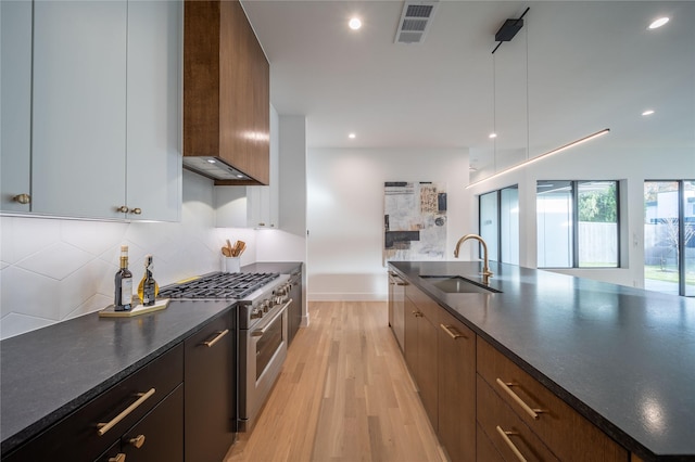 kitchen featuring pendant lighting, sink, wall chimney exhaust hood, light wood-type flooring, and stainless steel appliances