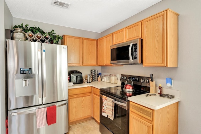 kitchen featuring light brown cabinets, stainless steel appliances, and a textured ceiling