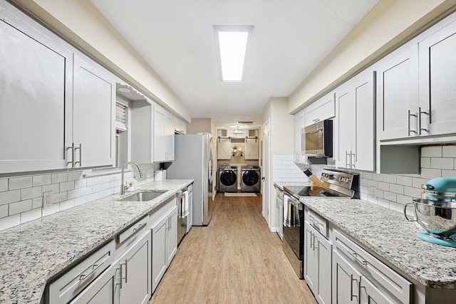 kitchen featuring sink, decorative backsplash, independent washer and dryer, light hardwood / wood-style floors, and stainless steel appliances