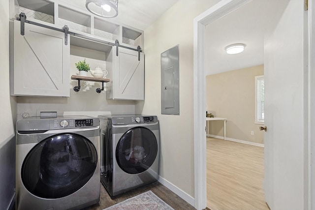 clothes washing area featuring cabinets, a barn door, electric panel, washer and dryer, and hardwood / wood-style flooring