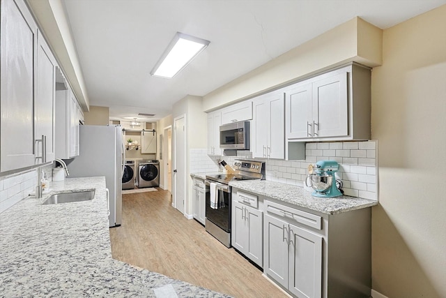 kitchen featuring backsplash, sink, independent washer and dryer, light hardwood / wood-style floors, and stainless steel appliances