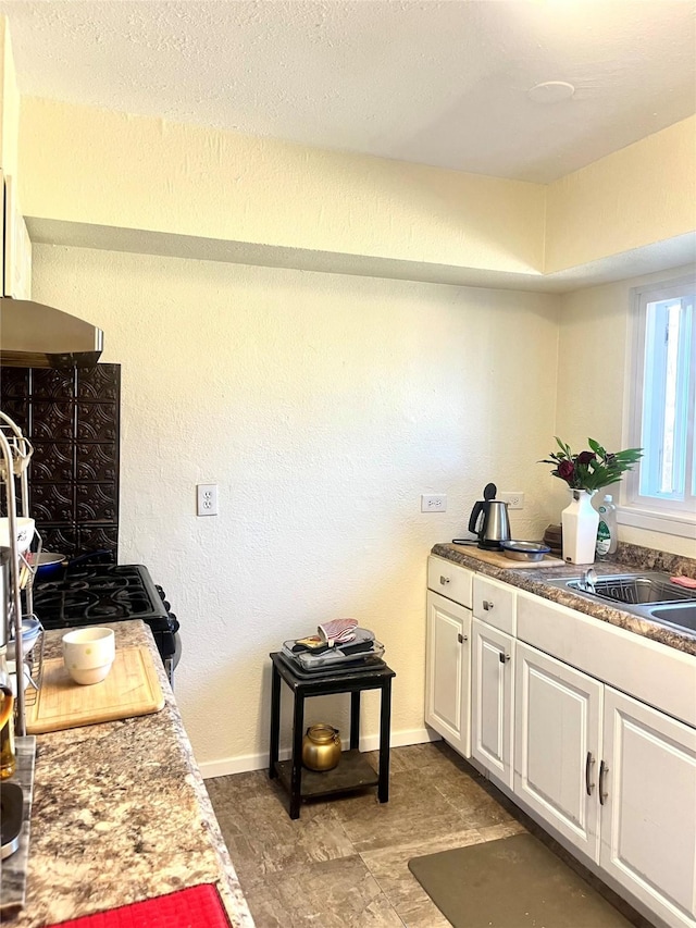 kitchen featuring baseboards, black gas range, white cabinets, under cabinet range hood, and a textured wall