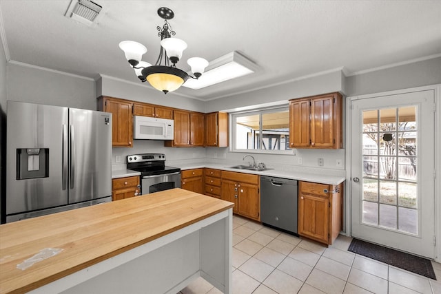 kitchen featuring sink, decorative light fixtures, light tile patterned floors, ornamental molding, and appliances with stainless steel finishes