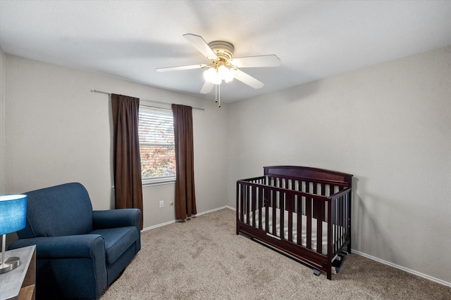 carpeted bedroom with a crib and ceiling fan