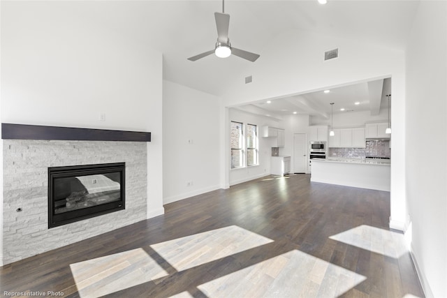 unfurnished living room featuring vaulted ceiling, dark hardwood / wood-style floors, a stone fireplace, and ceiling fan