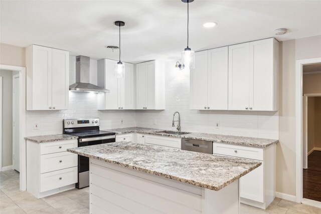 kitchen featuring appliances with stainless steel finishes, wall chimney exhaust hood, white cabinets, a kitchen island, and hanging light fixtures