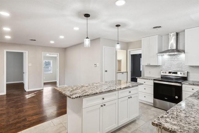 kitchen featuring a center island, wall chimney exhaust hood, stainless steel range with electric cooktop, light hardwood / wood-style floors, and white cabinets