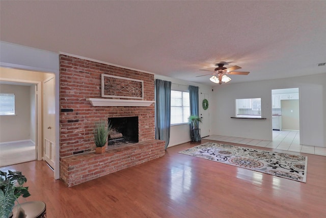 unfurnished living room featuring a fireplace, ceiling fan, light hardwood / wood-style flooring, and a textured ceiling