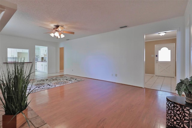 unfurnished living room featuring ceiling fan, ornamental molding, a textured ceiling, and light hardwood / wood-style flooring