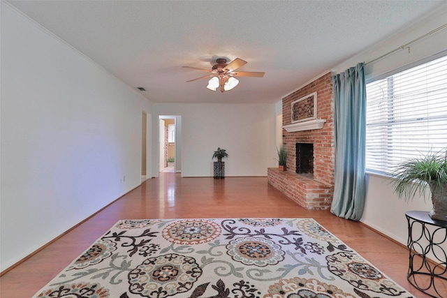 living room featuring a textured ceiling, light wood-type flooring, a brick fireplace, and ceiling fan