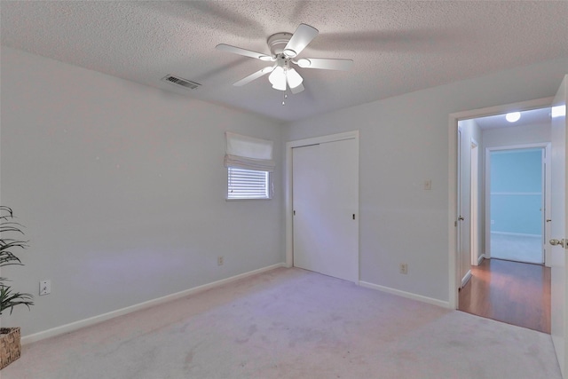 unfurnished bedroom featuring ceiling fan, light colored carpet, a textured ceiling, and a closet