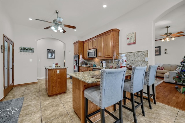 kitchen featuring kitchen peninsula, light stone countertops, backsplash, ceiling fan, and a kitchen island