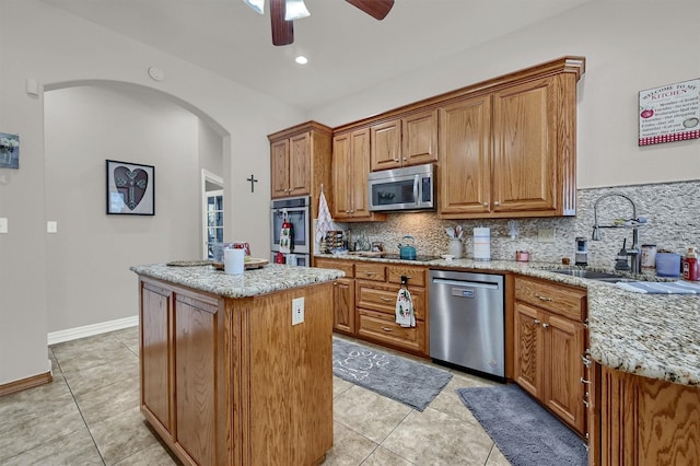 kitchen featuring a center island, sink, stainless steel appliances, tasteful backsplash, and light stone counters