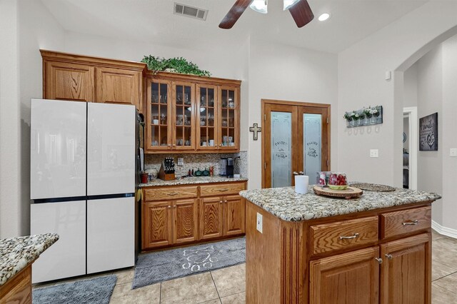 kitchen featuring ceiling fan, light tile patterned flooring, white refrigerator, decorative backsplash, and a kitchen island