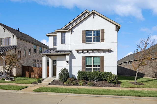 traditional-style house with brick siding, metal roof, a standing seam roof, fence, and a front yard