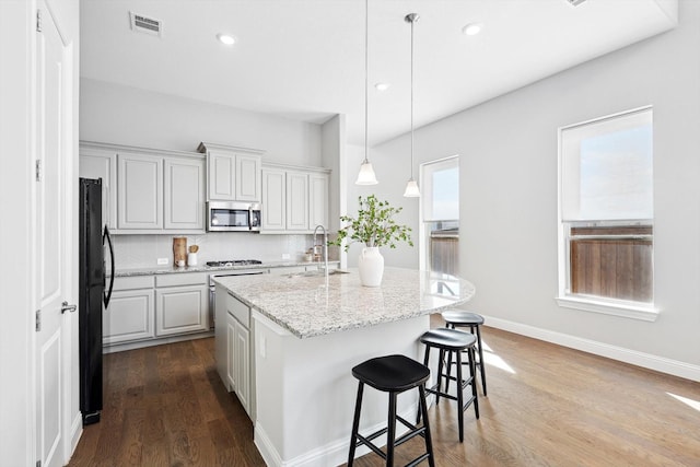 kitchen featuring light stone countertops, sink, hardwood / wood-style floors, a center island with sink, and appliances with stainless steel finishes