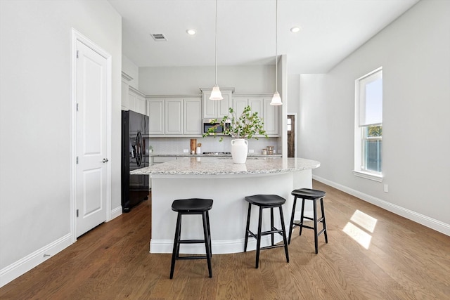 kitchen featuring decorative backsplash, light wood-type flooring, hanging light fixtures, and black refrigerator with ice dispenser