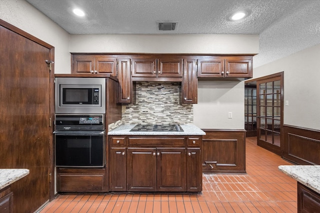 kitchen with dark brown cabinetry, light stone countertops, a textured ceiling, decorative backsplash, and black appliances