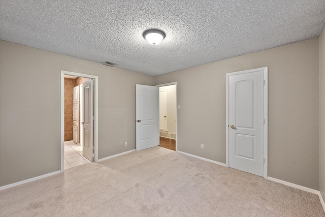 unfurnished bedroom with a textured ceiling, light carpet, connected bathroom, and a closet