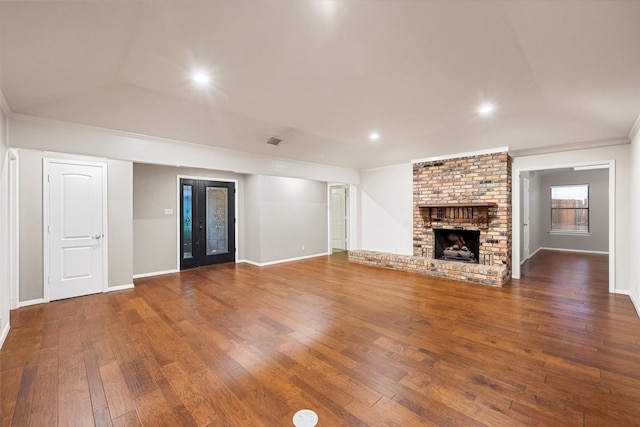 unfurnished living room with vaulted ceiling, dark hardwood / wood-style floors, ornamental molding, a brick fireplace, and french doors