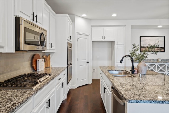 kitchen with dark stone countertops, white cabinetry, stainless steel appliances, and a sink