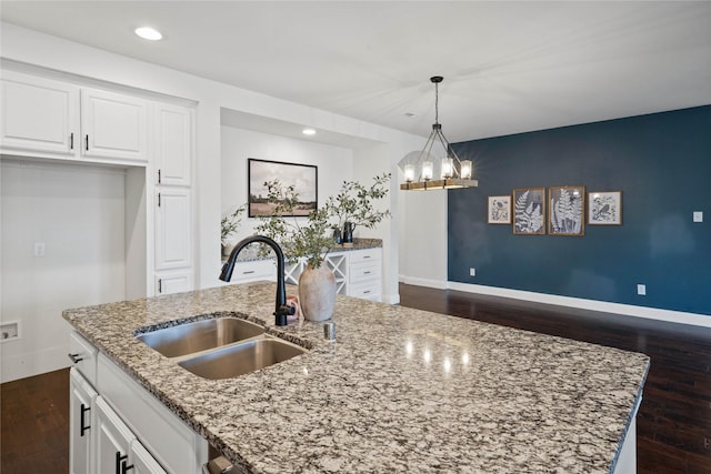 kitchen featuring a kitchen island with sink, a sink, white cabinetry, light stone countertops, and decorative light fixtures