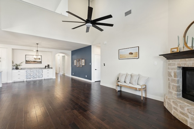 living room with ceiling fan, a fireplace, a high ceiling, and dark hardwood / wood-style floors