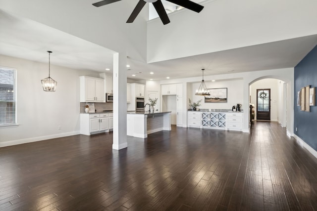 unfurnished living room with ceiling fan, sink, a towering ceiling, and dark wood-type flooring