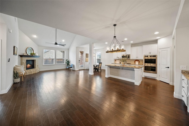 kitchen featuring an island with sink, appliances with stainless steel finishes, open floor plan, light stone counters, and decorative light fixtures