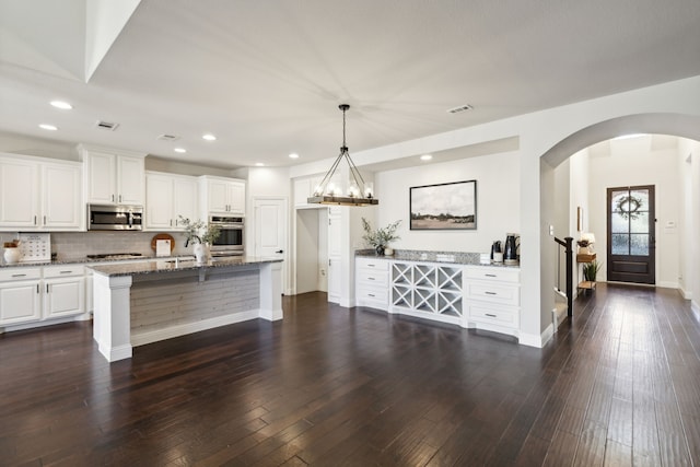 kitchen featuring light stone countertops, appliances with stainless steel finishes, dark hardwood / wood-style flooring, white cabinets, and hanging light fixtures