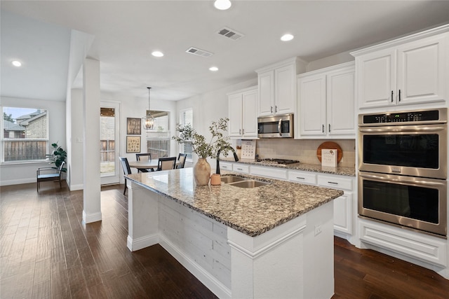 kitchen featuring light stone counters, a center island with sink, visible vents, appliances with stainless steel finishes, and white cabinets