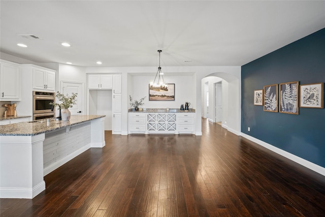 kitchen with stone counters, arched walkways, visible vents, hanging light fixtures, and white cabinetry