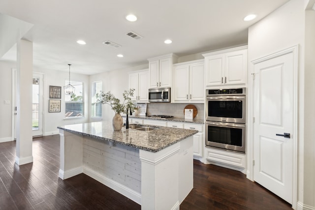 kitchen with stainless steel appliances, a kitchen island with sink, stone countertops, white cabinets, and dark hardwood / wood-style floors