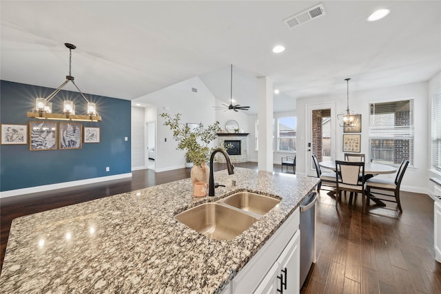 kitchen featuring light stone counters, a sink, visible vents, white cabinets, and open floor plan