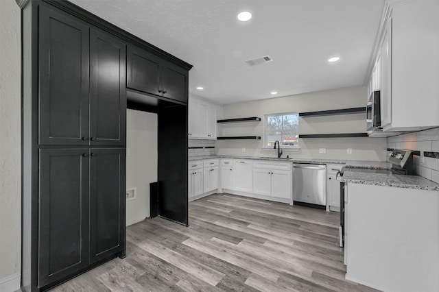 kitchen with white cabinets, appliances with stainless steel finishes, tasteful backsplash, sink, and light hardwood / wood-style flooring